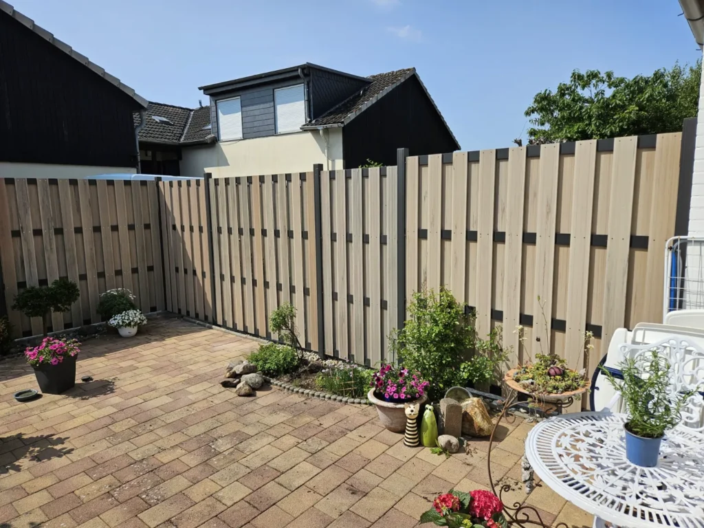 Moderner Holzzaun und gepflasterte Terrasse in einem sonnigen Garten, der Privatsphäre und Ästhetik vereint.