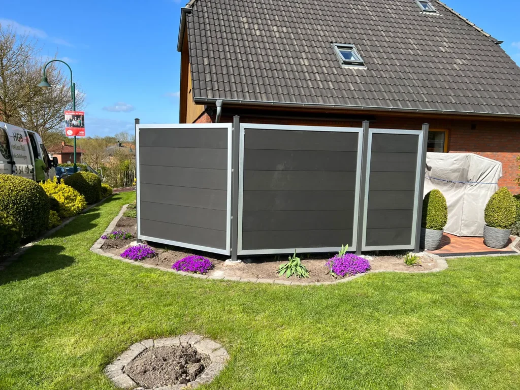 Moderner, dunkelgrauer Sichtschutz aus WPC-Paneelen mit silbernen Rahmen, installiert von HGB Holz und Gartenbau nach einer Rasenpflege im Frühjahr