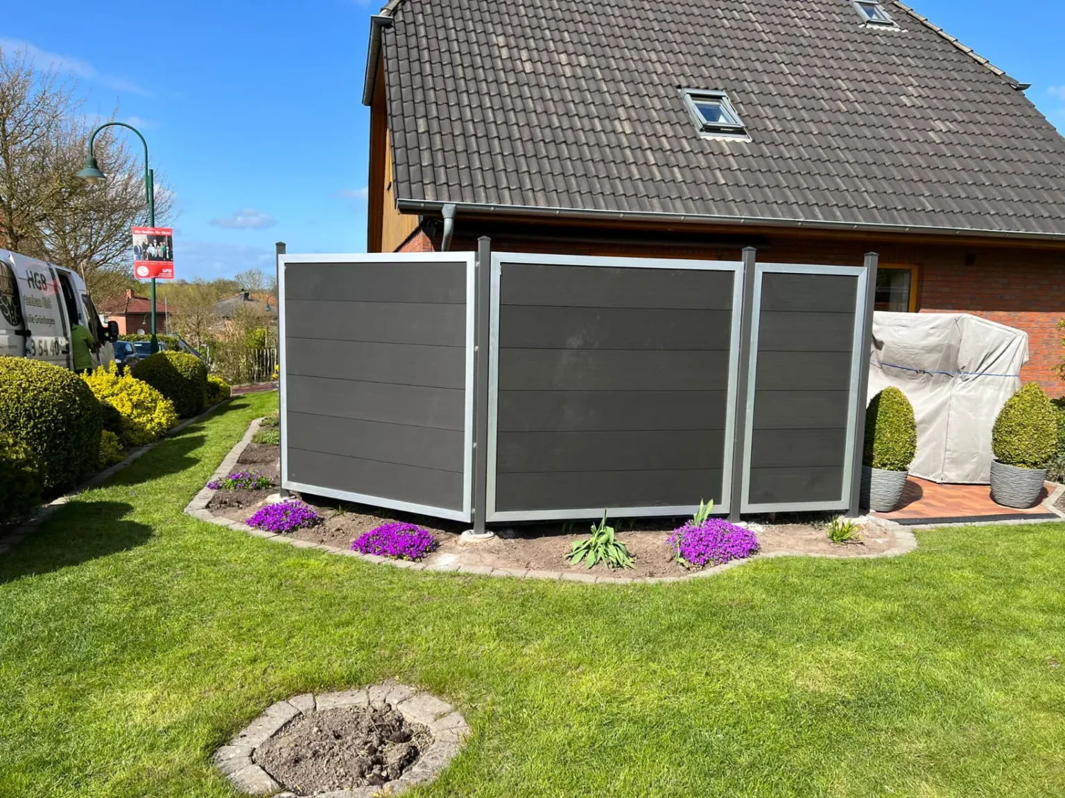 Moderner, dunkelgrauer Sichtschutz aus WPC-Paneelen mit silbernen Rahmen, installiert von HGB Holz und Gartenbau nach einer Rasenpflege im Frühjahr