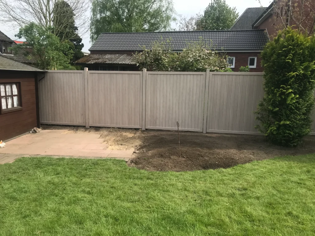 Ein neu installierter, heller Sichtschutzzaun aus Holz oder WPC in einem Garten mit Rasen, Terrasse und einem Gartenhaus.