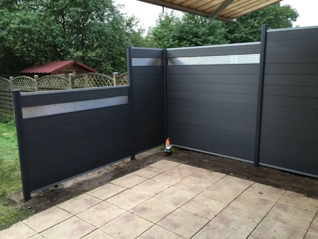 Moderner, dunkelgrauer Sichtschutz mit perforiertem Metallstreifen auf einer Terrasse in Stockelsdorf, im Hintergrund ein Garten.
